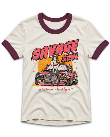 An off-white ringer t-shirt with dark maroon collar and sleeve cuffs, featuring a retro-style graphic of a woman in a white dress standing on a pink car with the text 'SAVAGE SOUL' and 'artrea design' printed below.