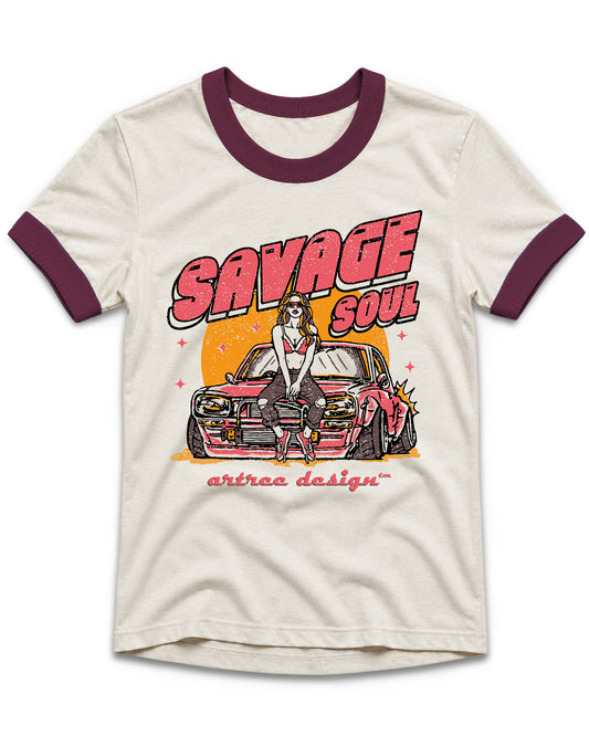 An off-white ringer t-shirt with dark maroon collar and sleeve cuffs, featuring a retro-style graphic of a woman in a white dress standing on a pink car with the text 'SAVAGE SOUL' and 'artrea design' printed below.