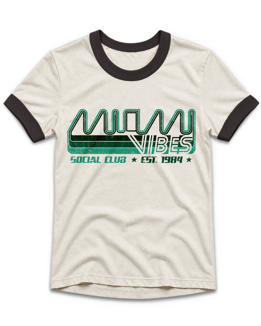 An off-white ringer t-shirt with black ribbed collar and sleeve cuffs, featuring a green and black graphic print on the front that reads 'MIAMI VIBES SOCIAL CLUB EST. 1984'.